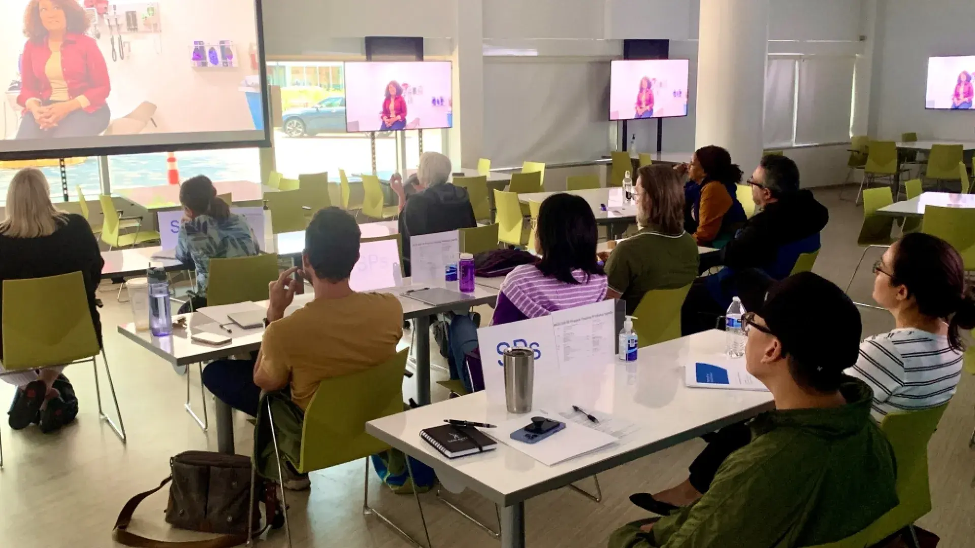 People sitting at tables facing a screen watch a video