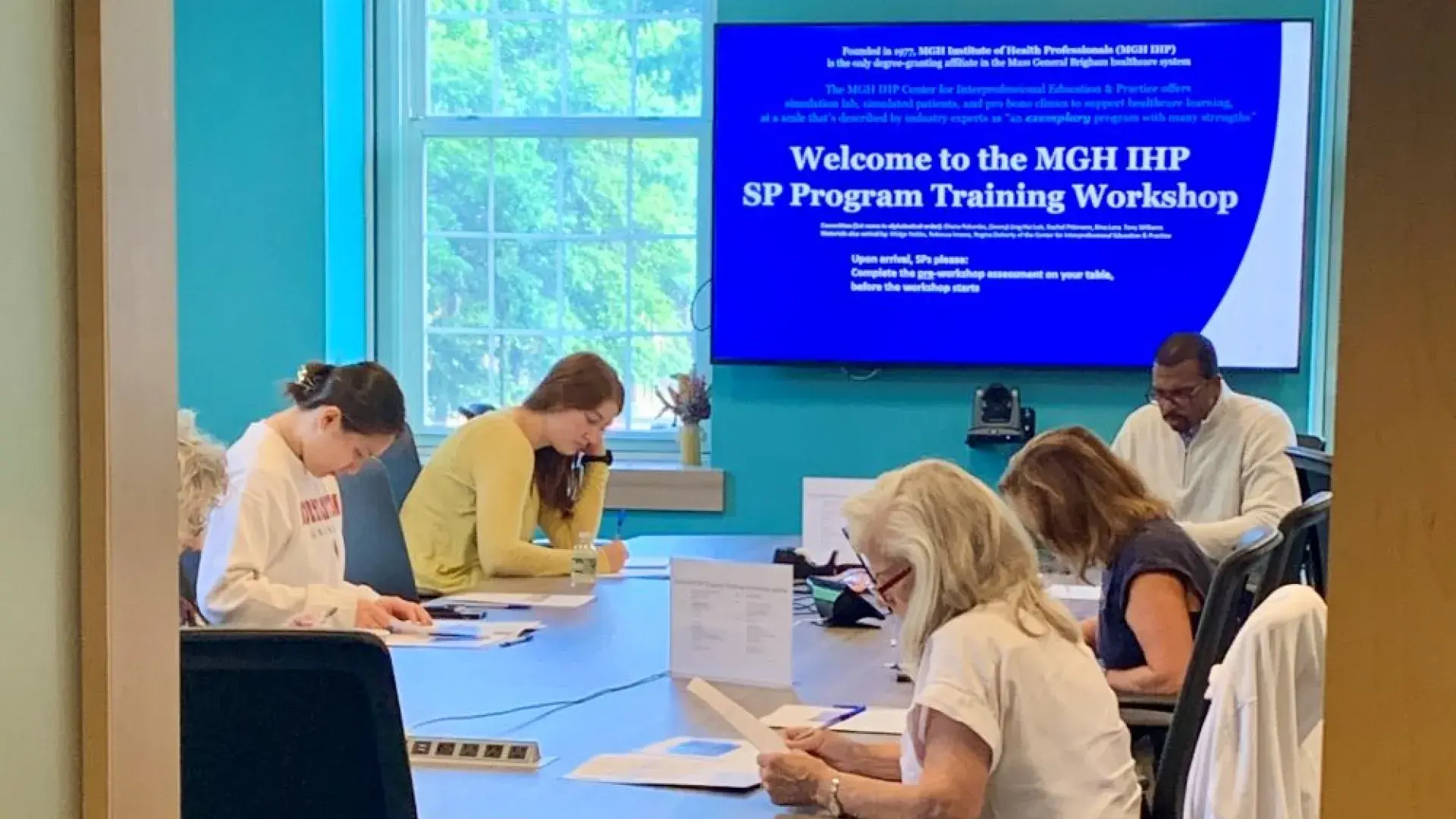 People sit around a table with a screen at one end 