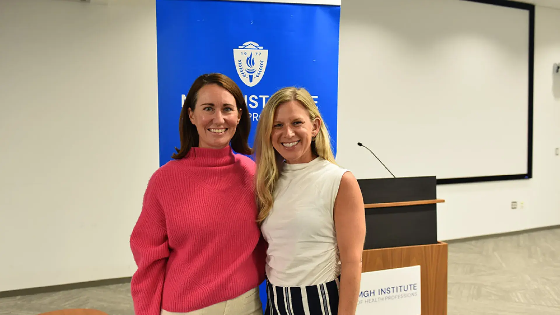 Two women stand in front of a blue back drop