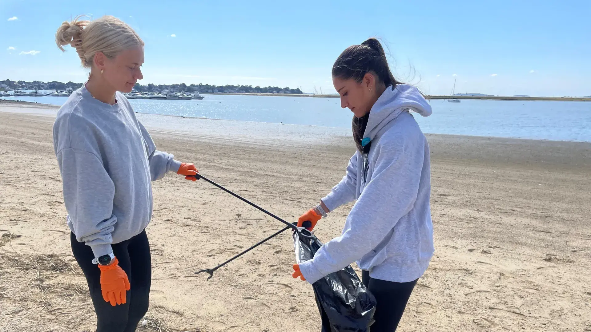 Two women on a beach pick up trash