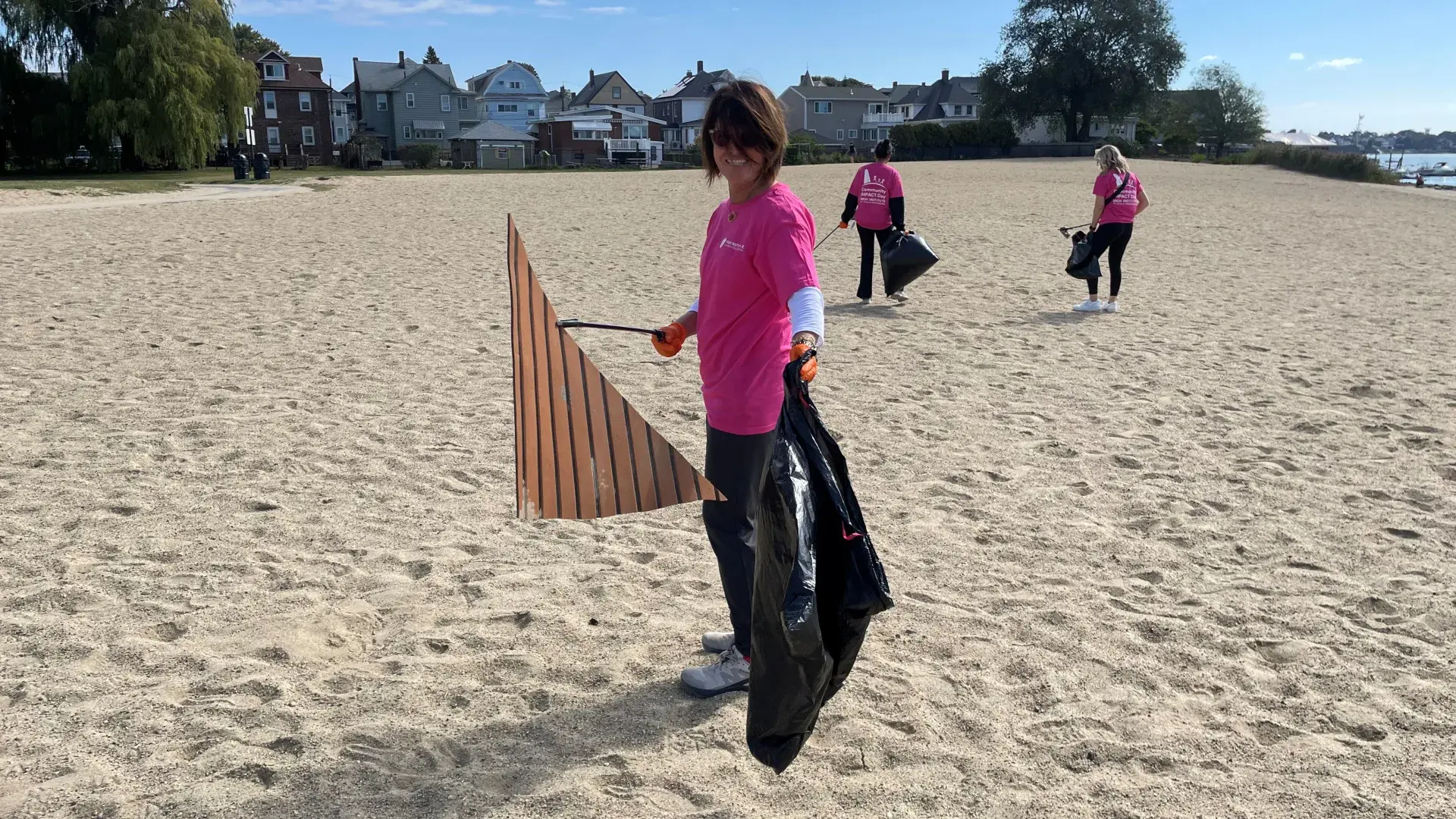 A woman holds a large piece of plastic and a garbage bag on a beach