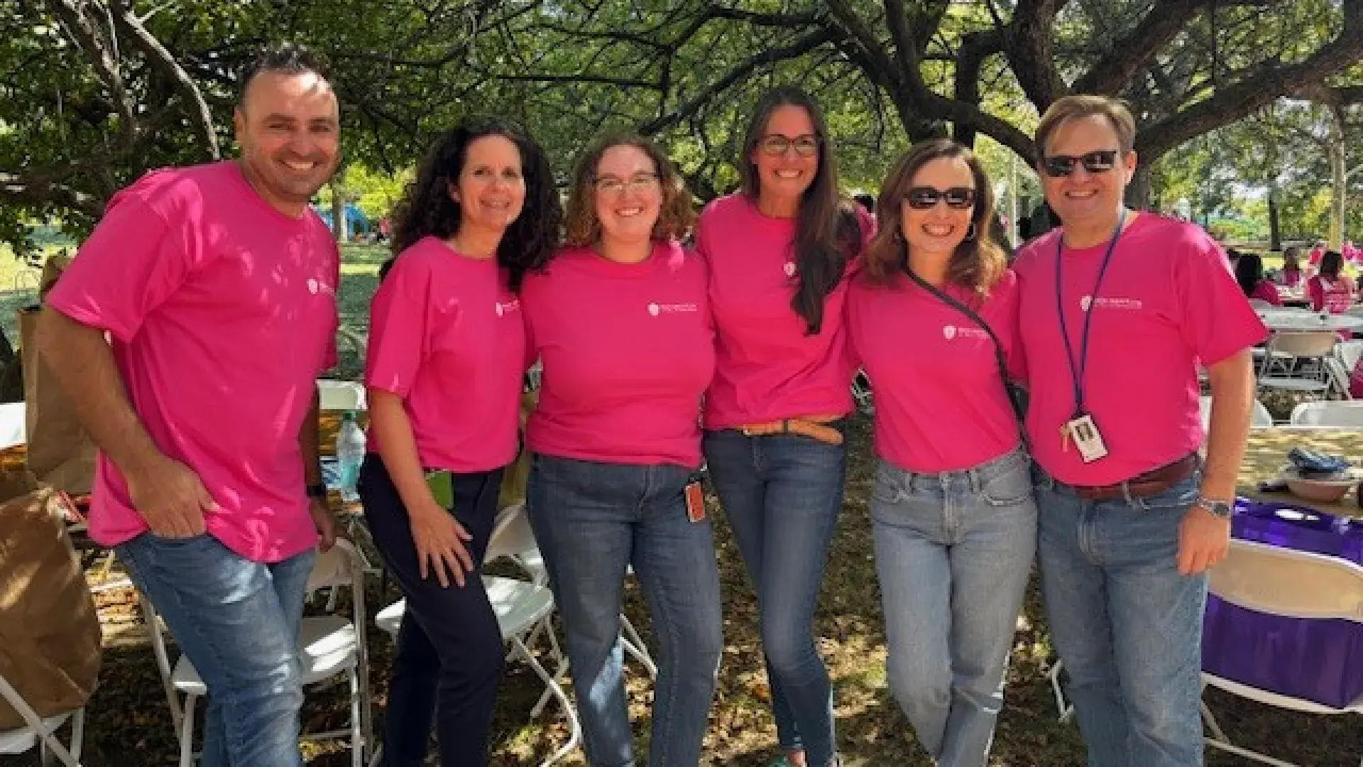 Six people pose for the camera next to tables and chairs outside
