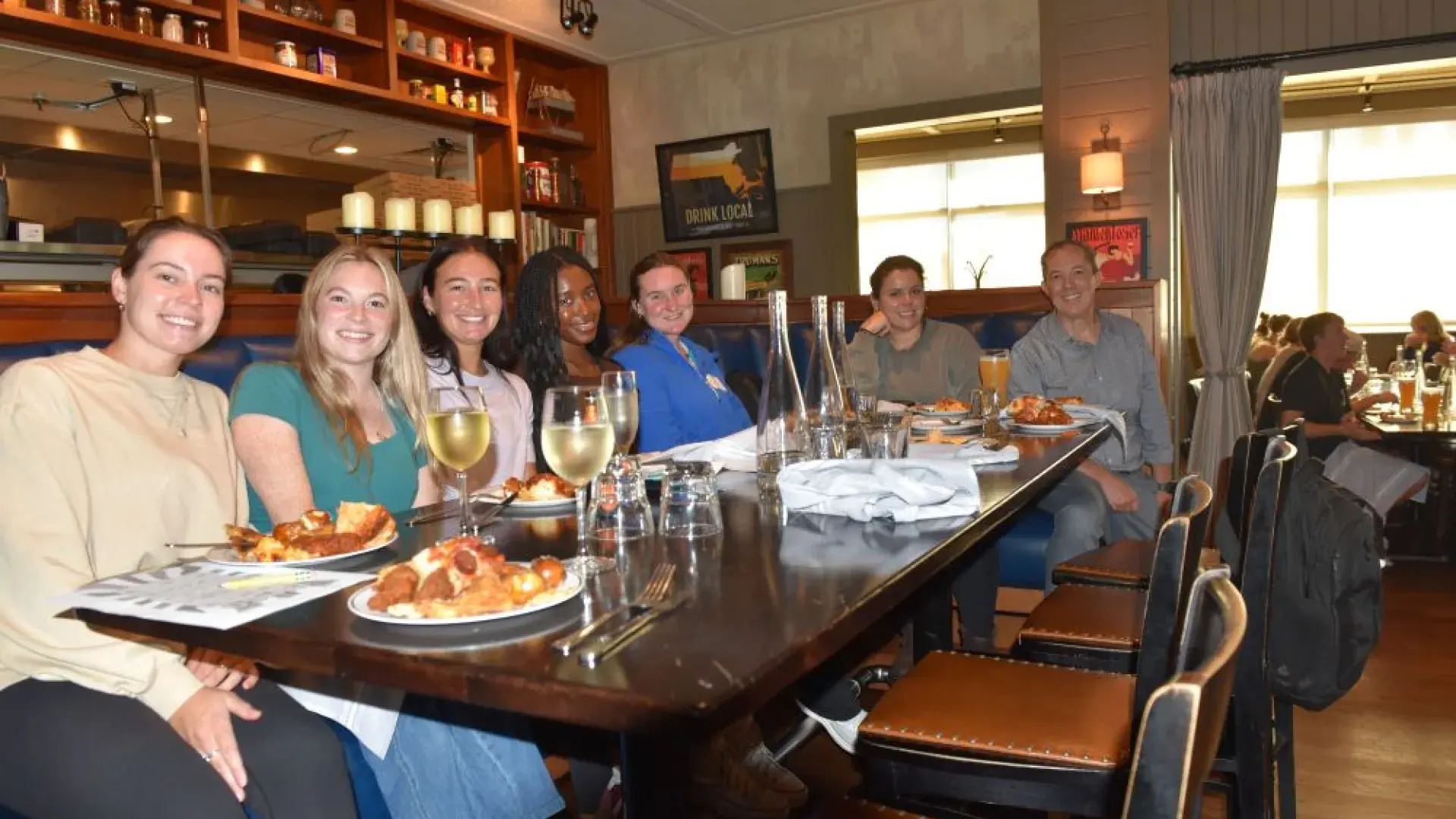 Seven people sit around a table with food and drinks at a restaurant