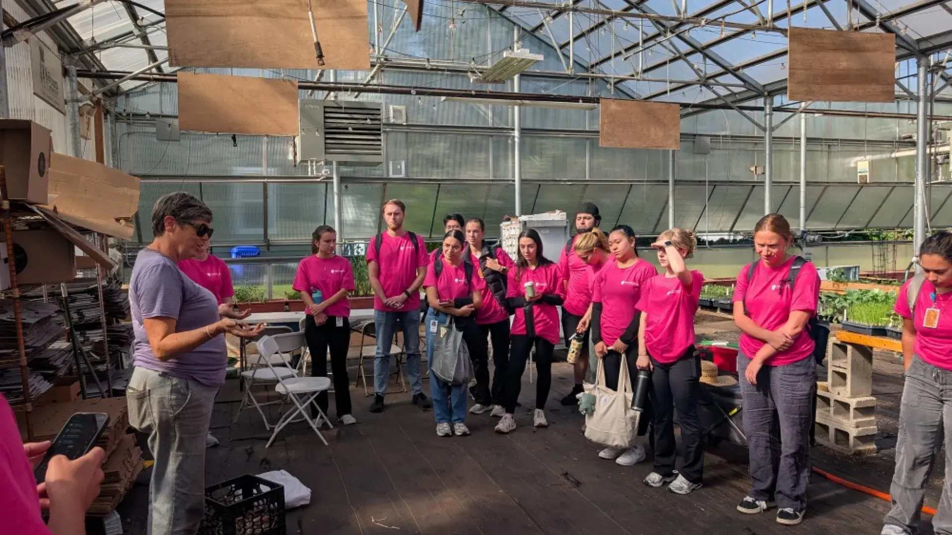 A group listens to someone talking while standing in a greenhouse