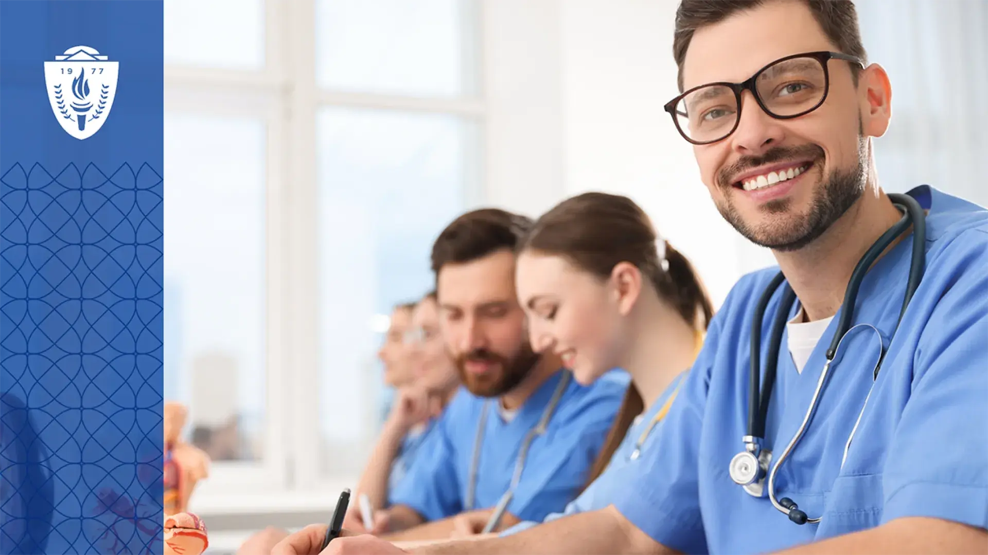 Group of physician assistants wearing stethoscopes and blue scrubs sitting at table