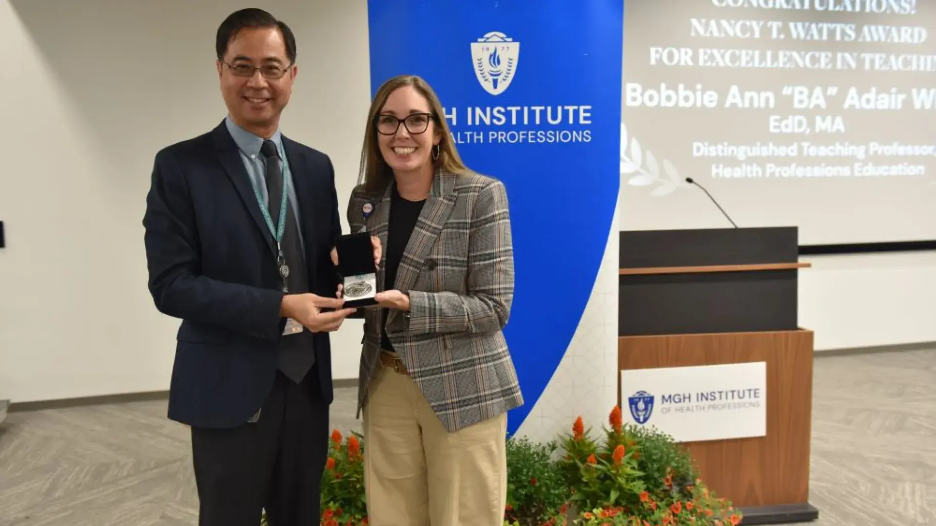 Man and woman holding a small box in front of a backdrop