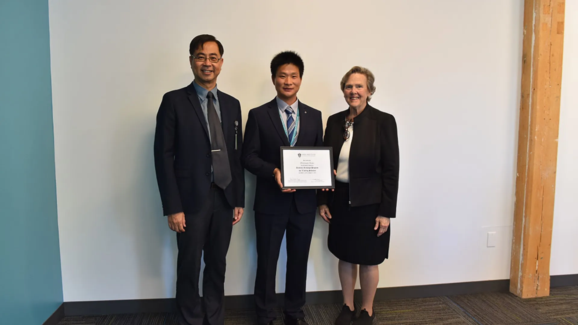 Three people pose against a white wall