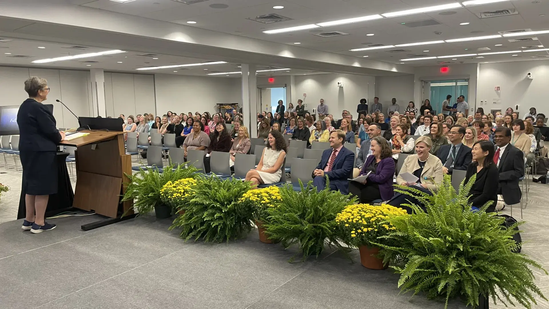 woman at a podium speaking to a mixed crowd