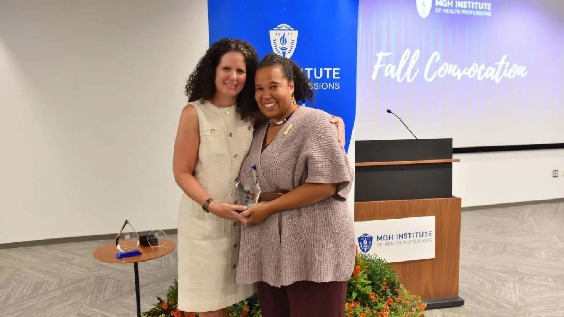 Two women in front of a backdrop holding award