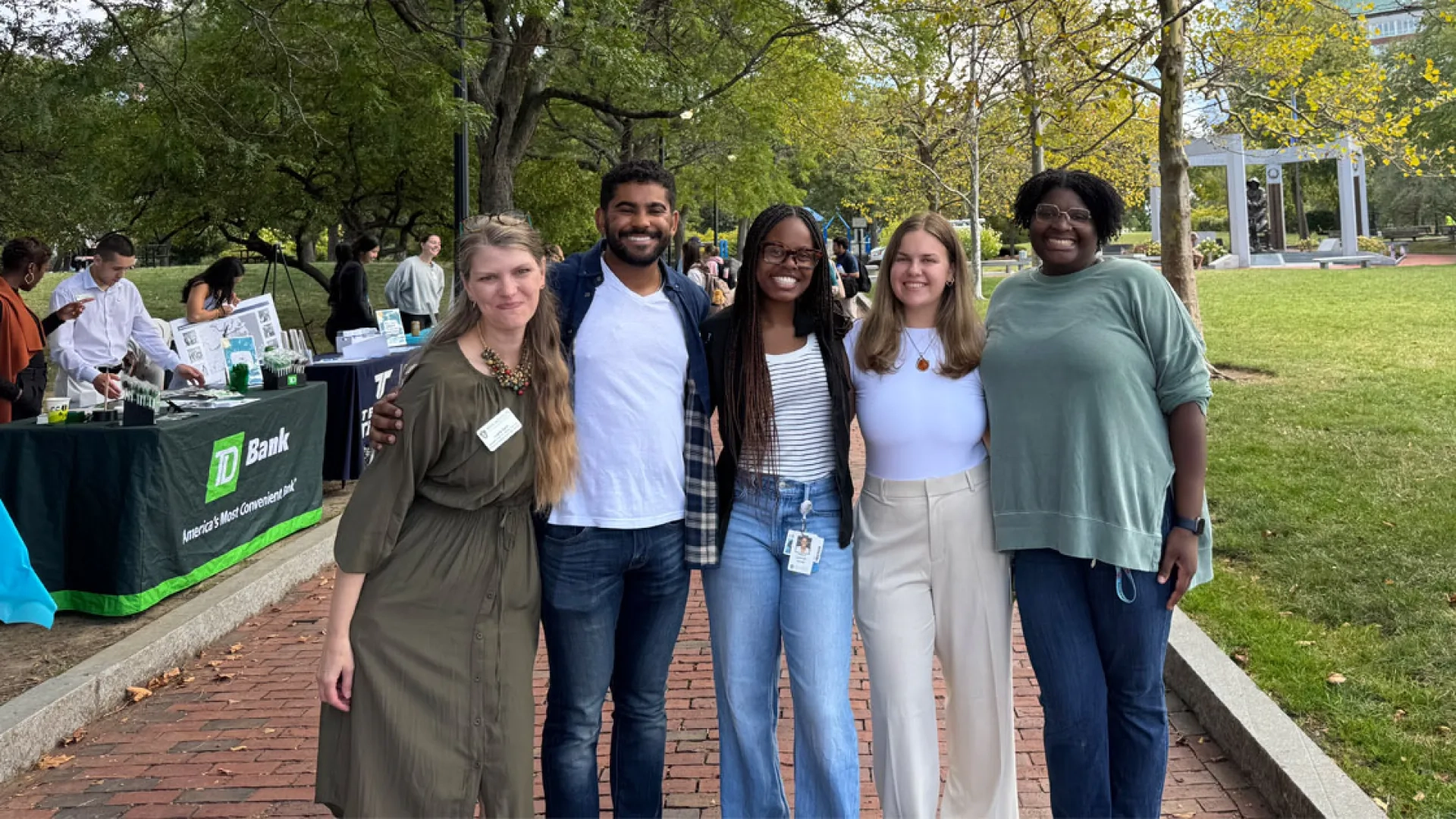 5 people standing on a brick path in front of trees huddles together