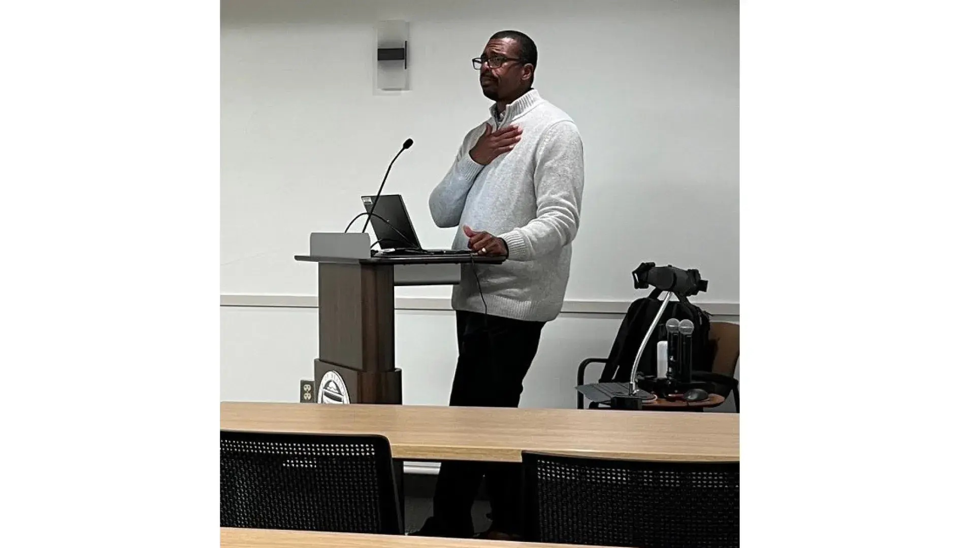 A man stands at a podium with his hand on his chest