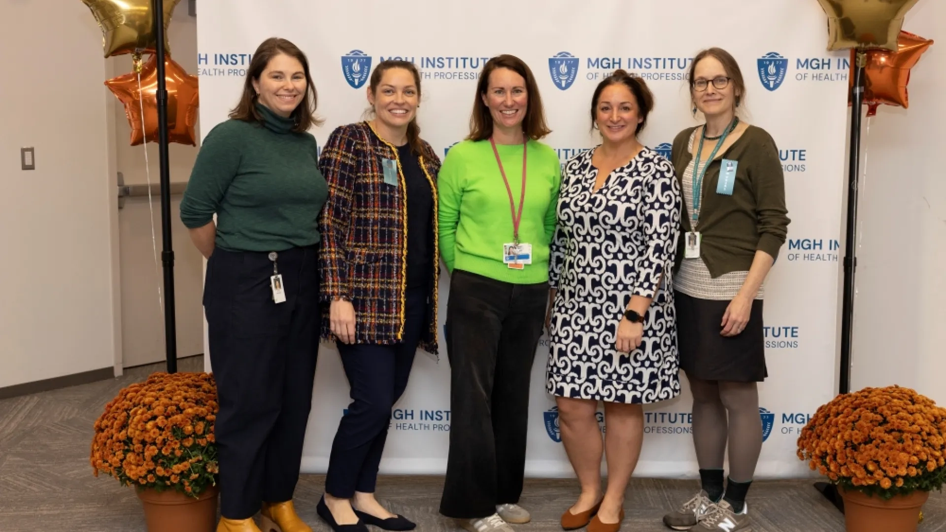 Five women stand against a backdrop posing for a photo
