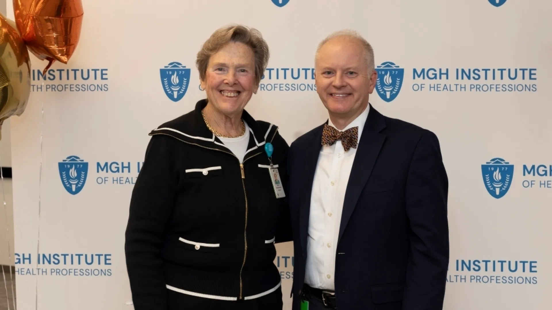 Two people pose in front of an MGH Institute backdrop
