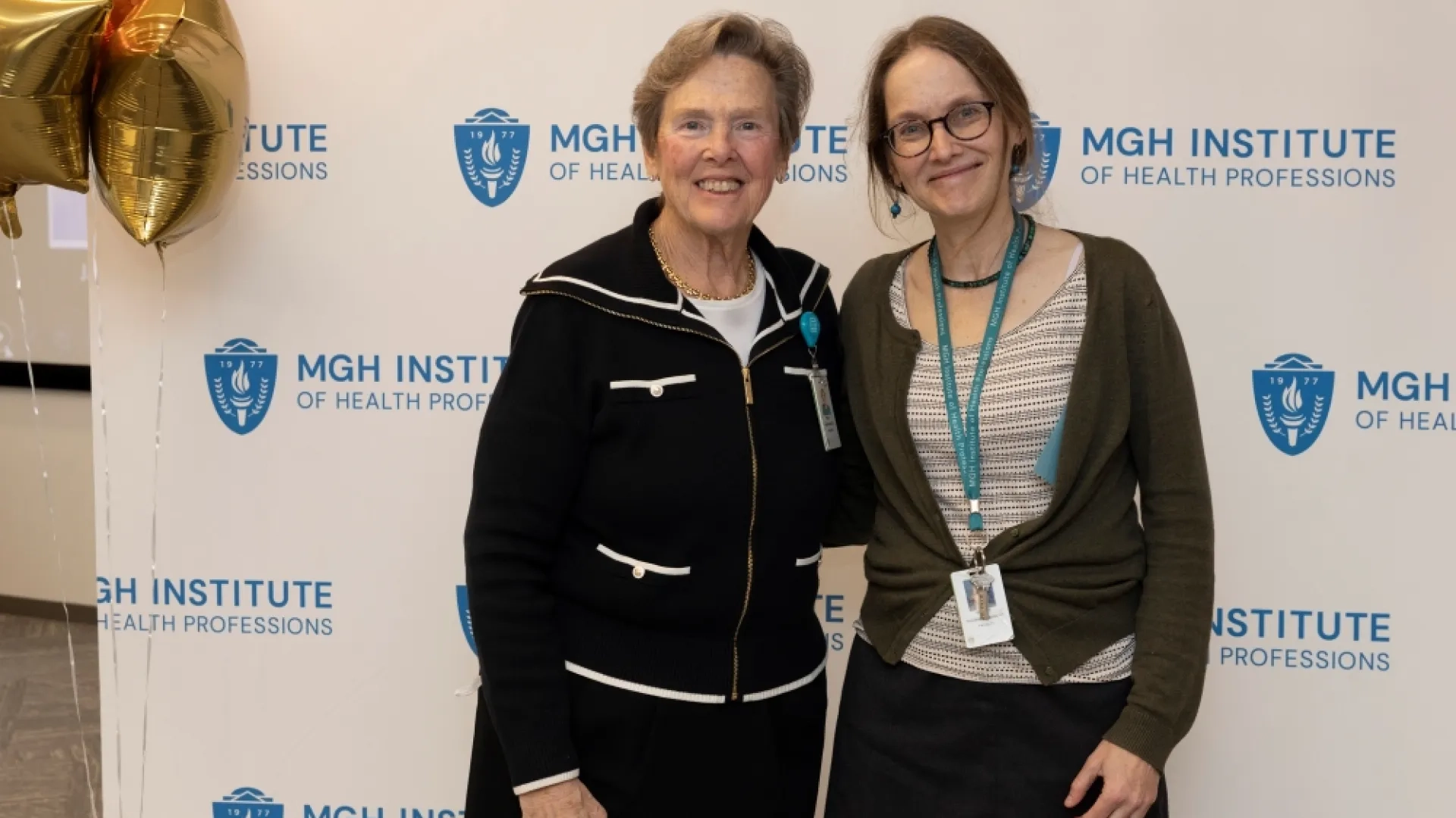 Two people pose in front of an MGH Institute backdrop