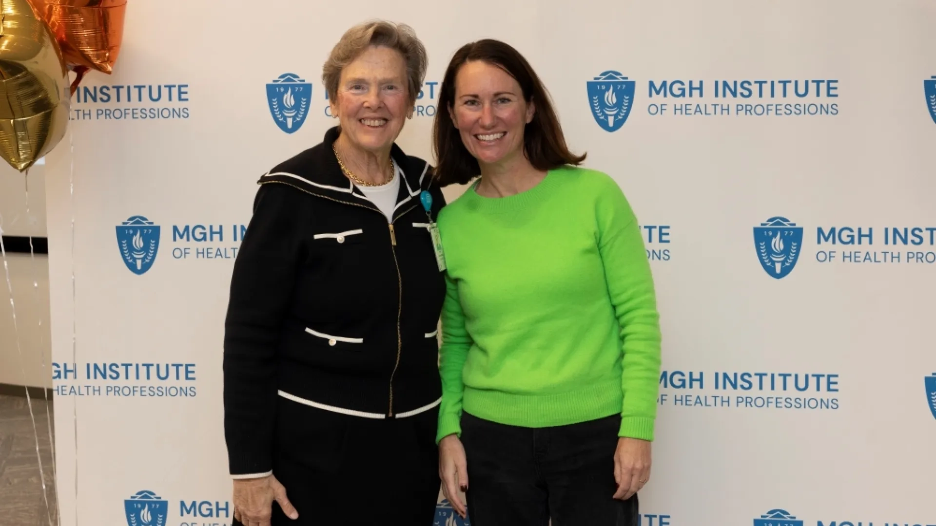 Two people pose in front of an MGH Institute backdrop