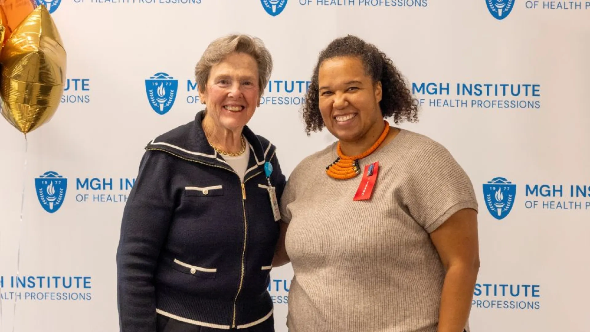 Two people pose in front of an MGH Institute backdrop