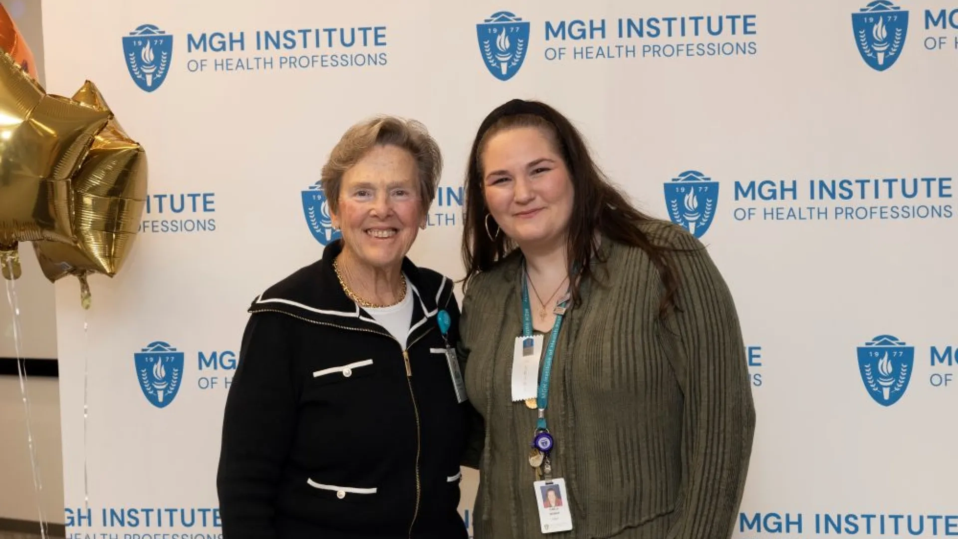 Two people pose in front of an MGH Institute backdrop