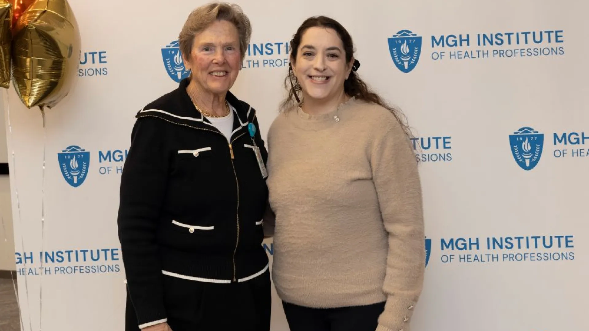 Two people pose in front of an MGH Institute backdrop