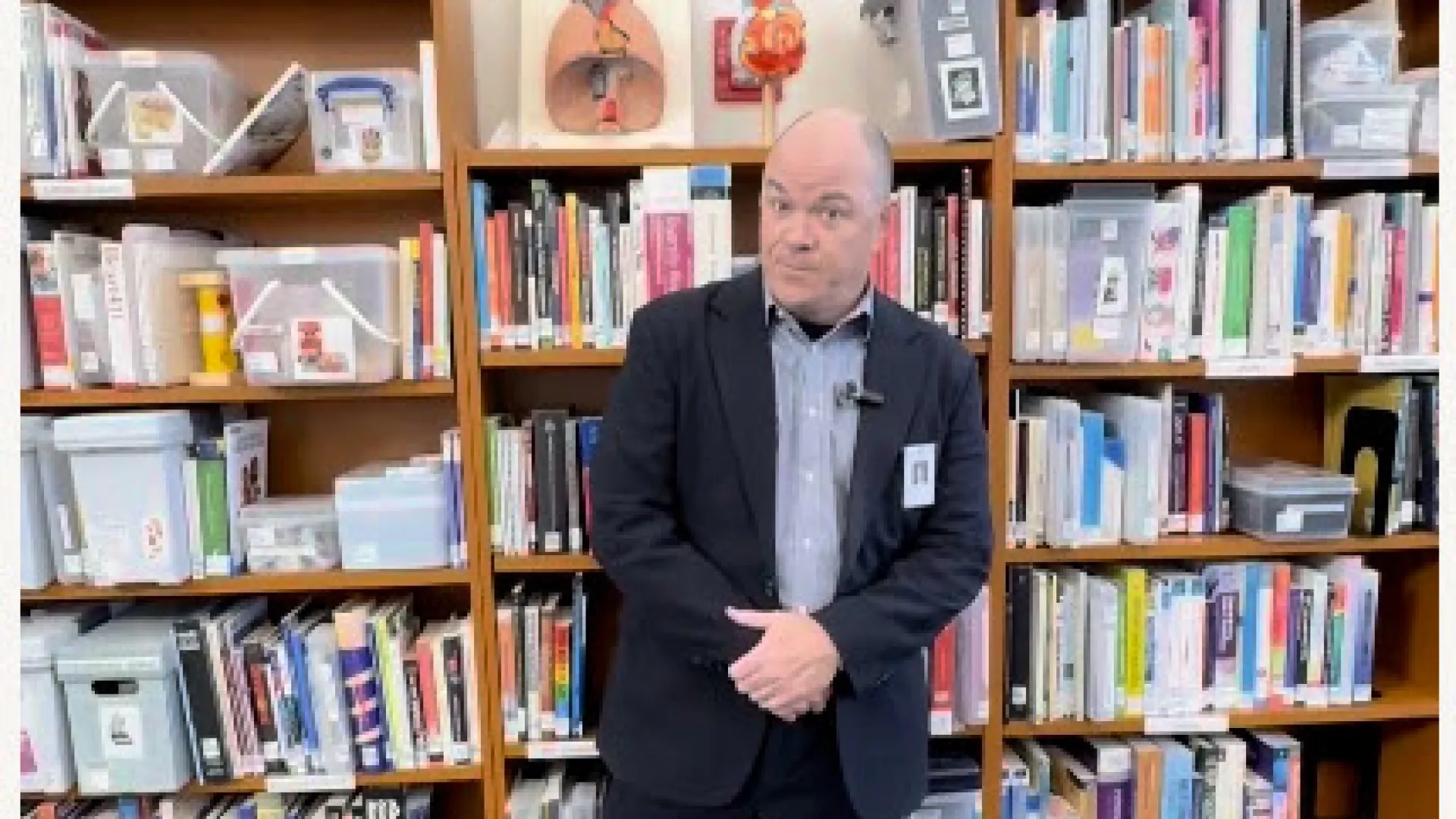 dave stands in front of a colorful bookshelf
