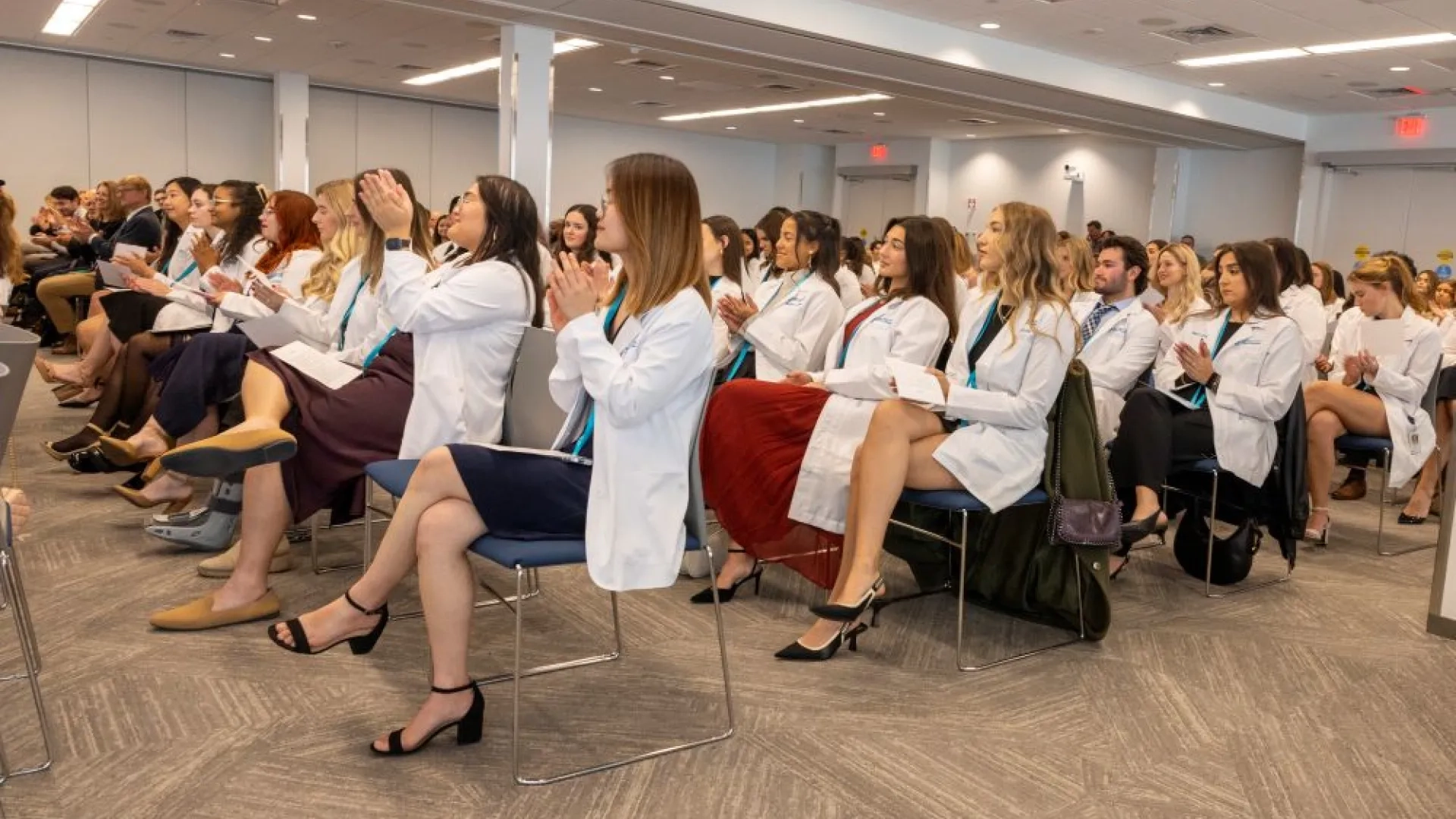 An audience of people in white coats sits in rows