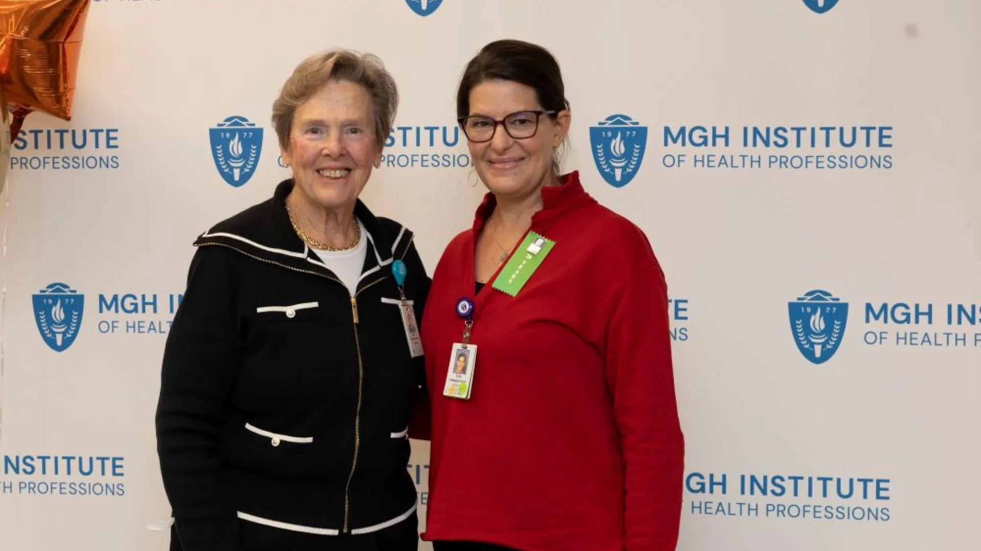 Two people pose in front of an MGH Institute backdrop