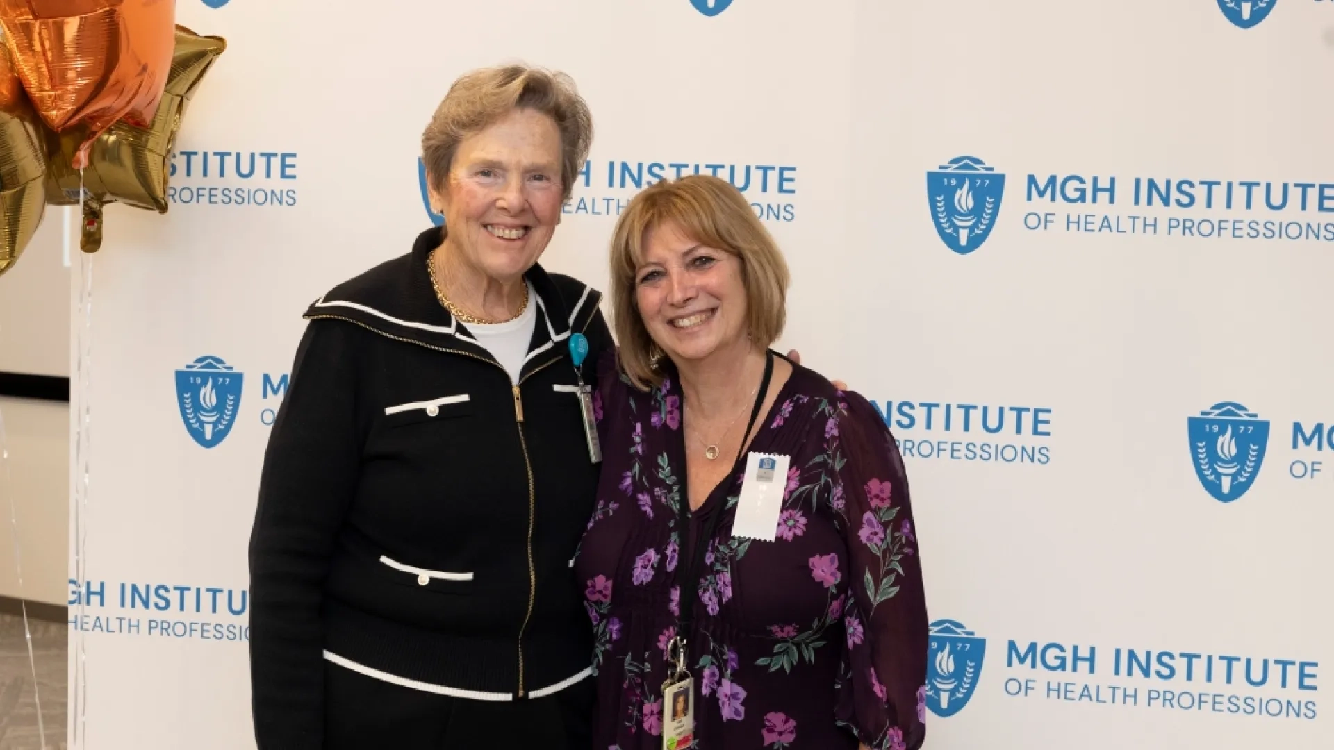 Two people pose in front of an MGH Institute backdrop