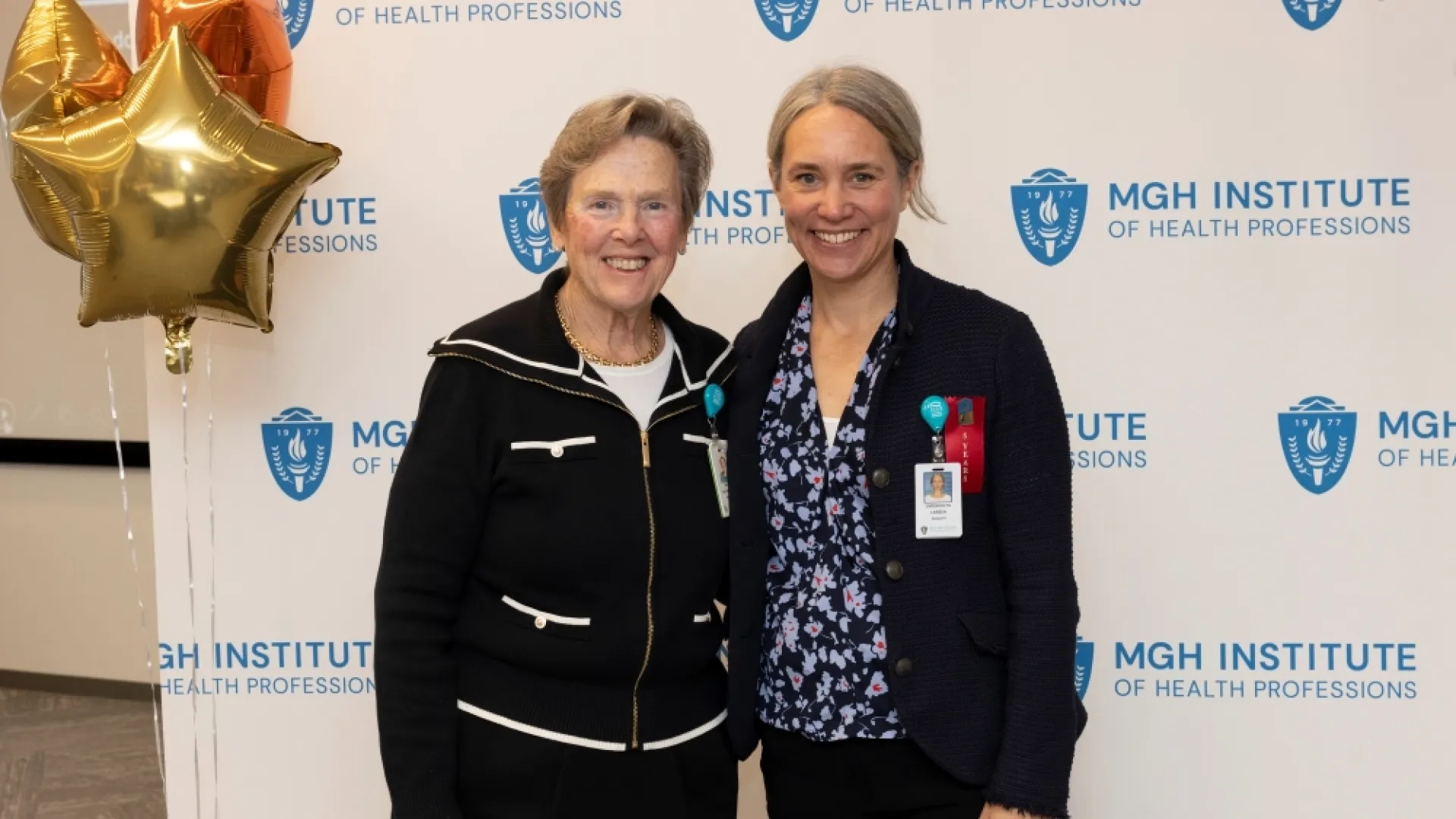 Two people pose in front of an MGH Institute backdrop