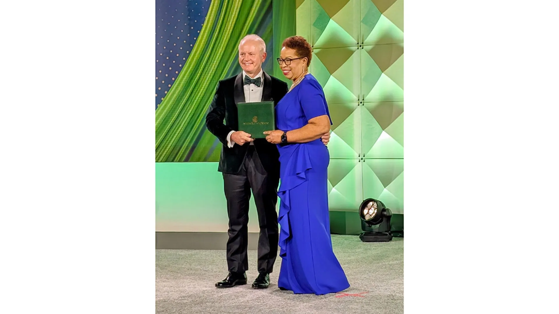 A woman hands a man a green folder while posing for photos