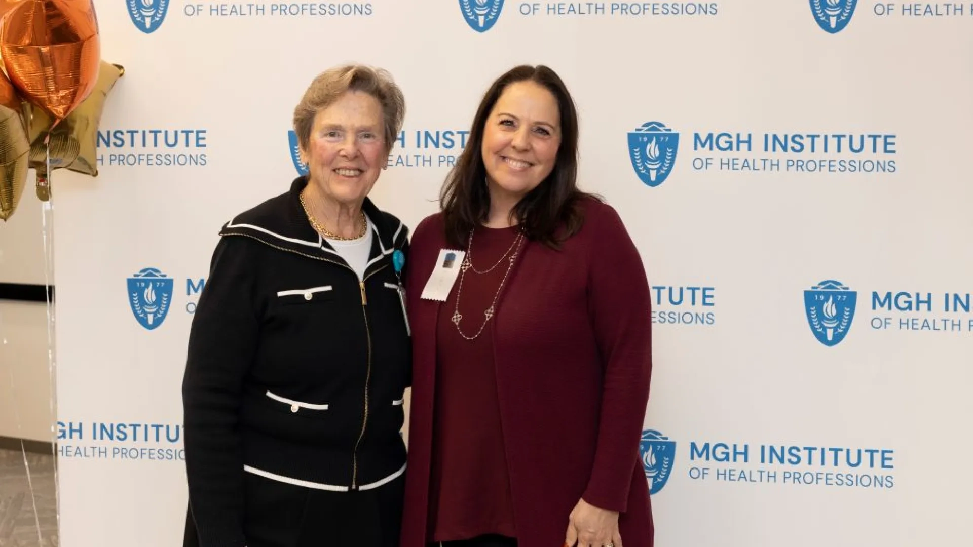 Two people pose in front of an MGH Institute backdrop
