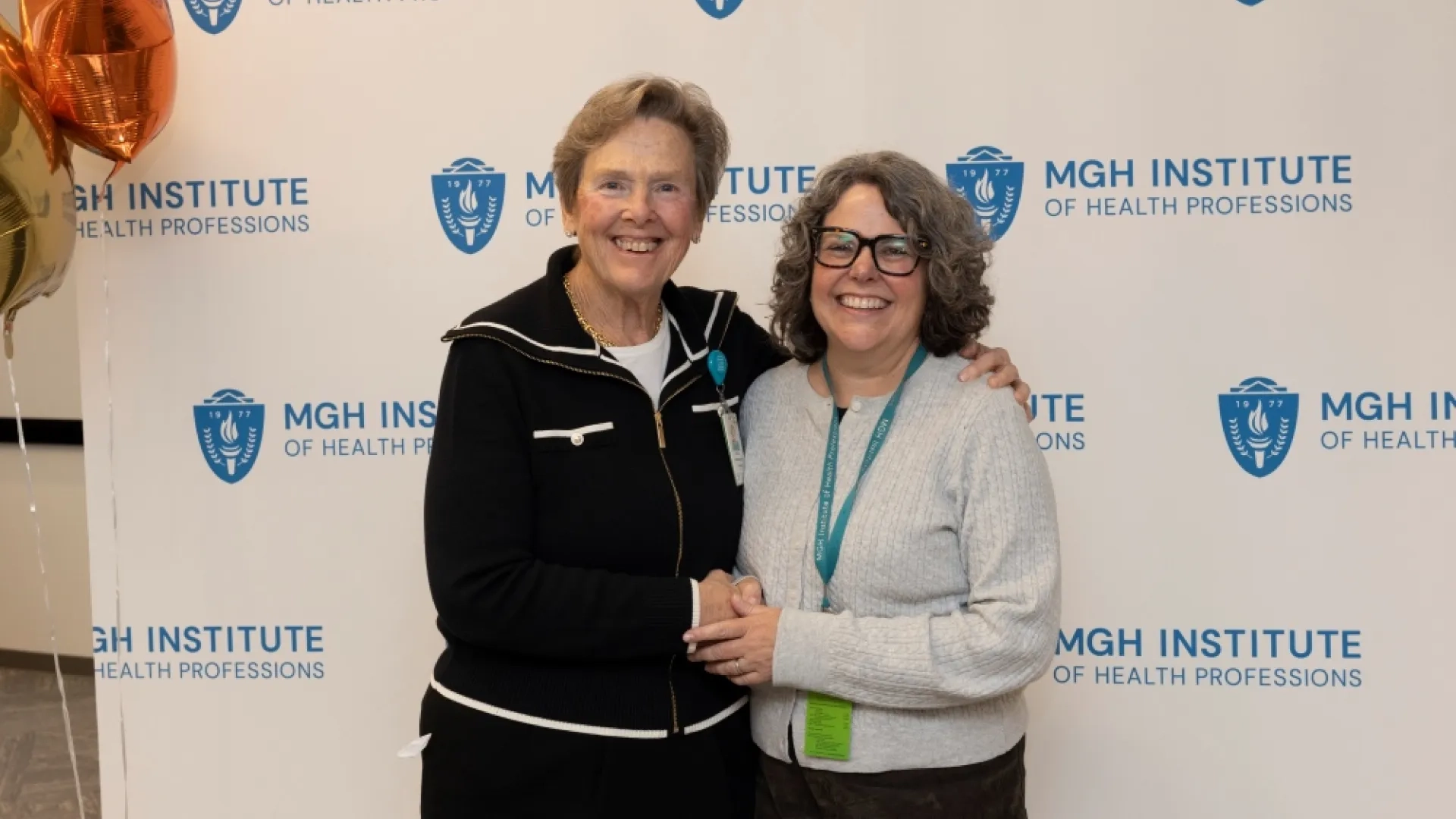 Two people pose in front of an MGH Institute backdrop