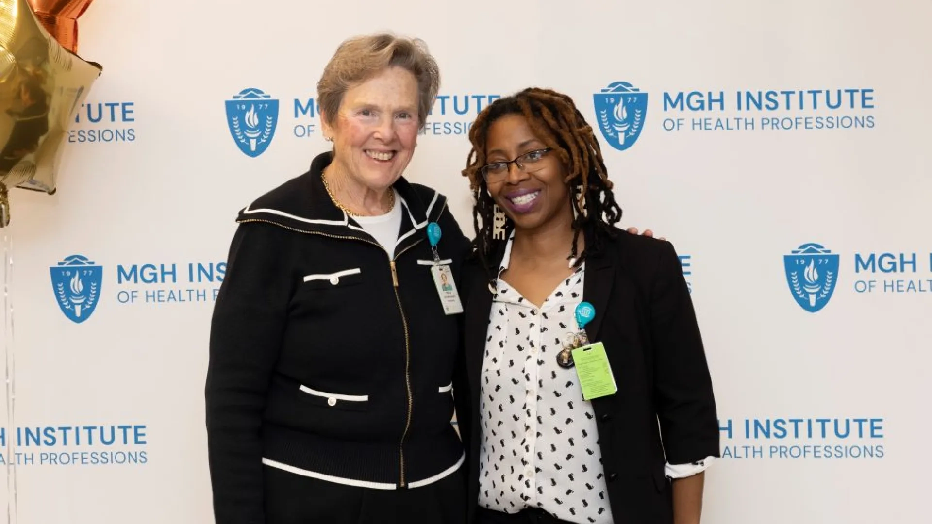 Two people pose in front of an MGH Institute backdrop