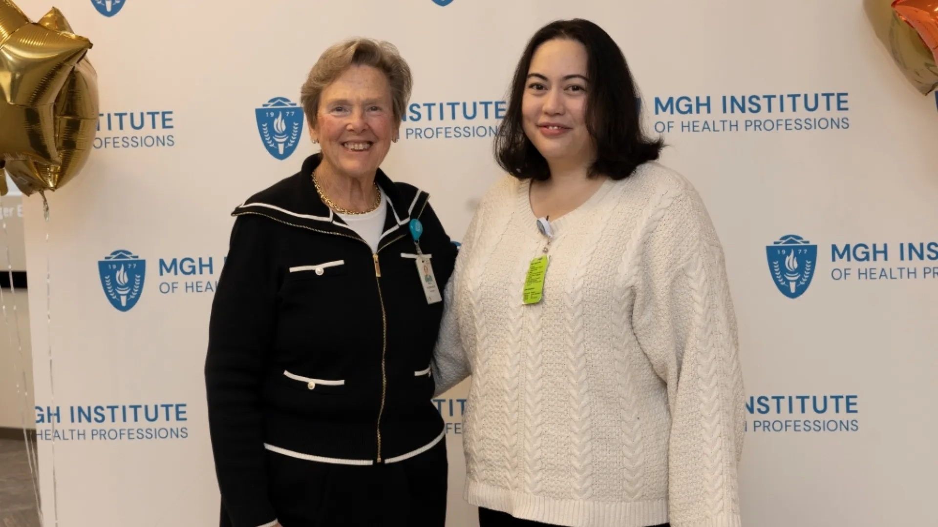 Two people pose in front of an MGH Institute backdrop