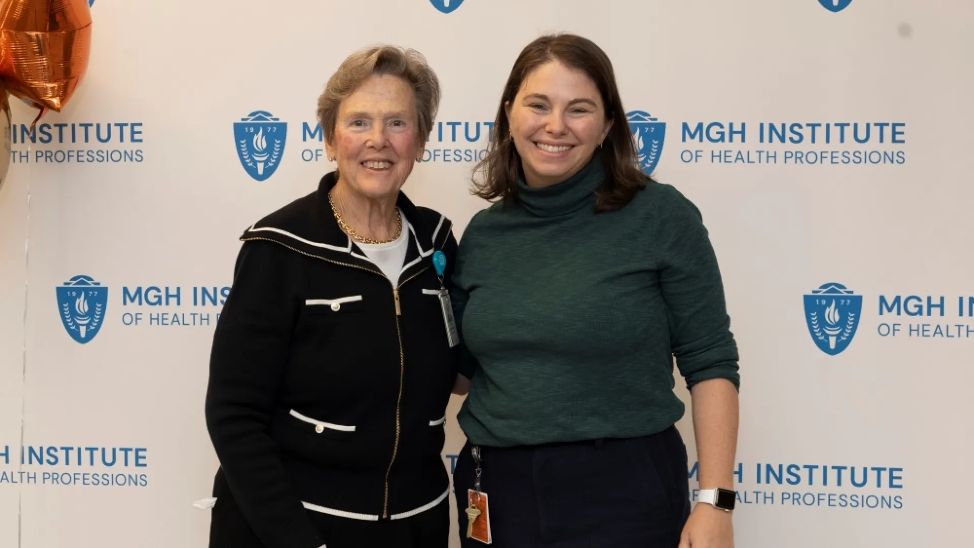 Two people pose in front of an MGH Institute backdrop