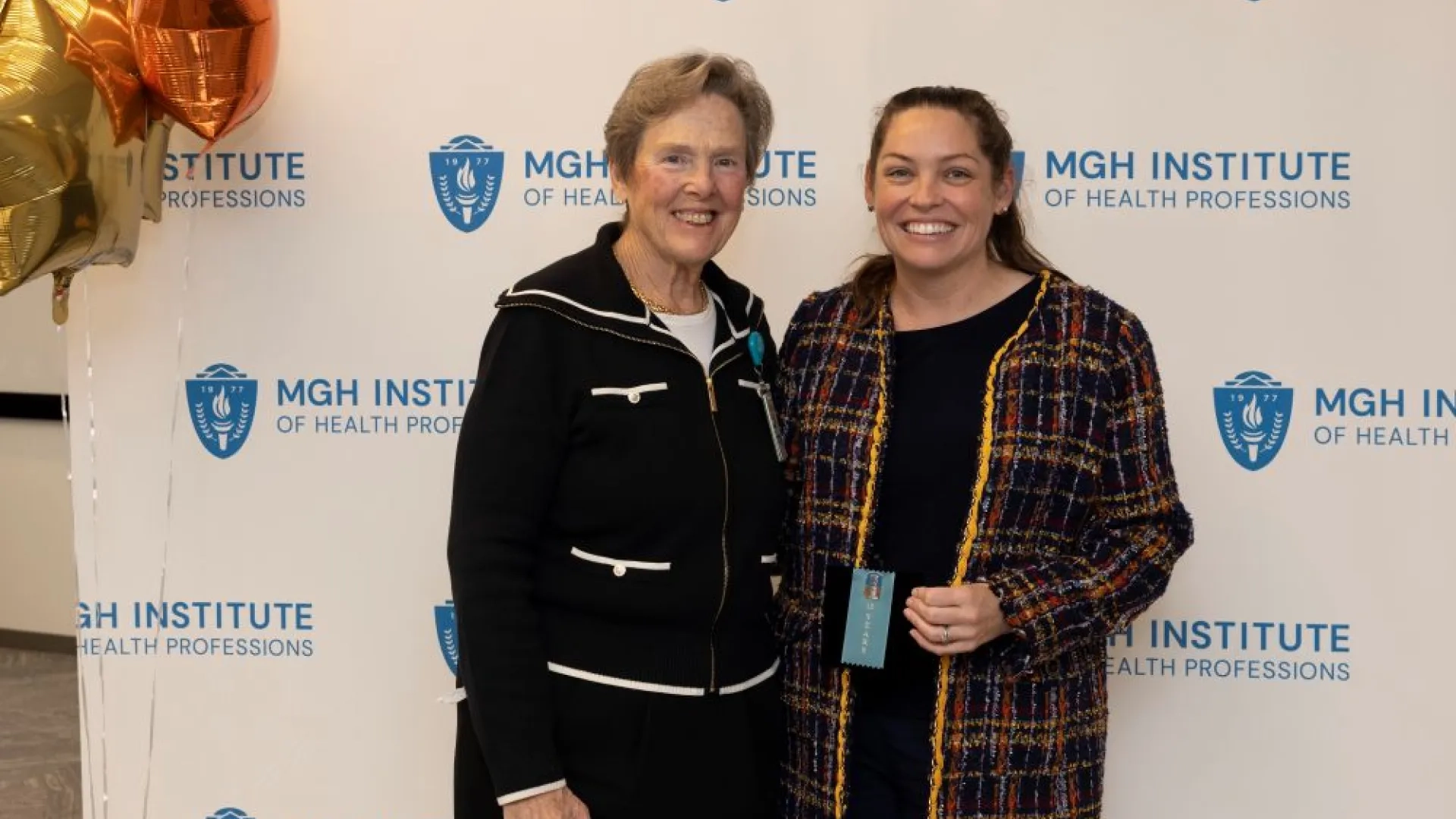 Two people pose in front of an MGH Institute backdrop