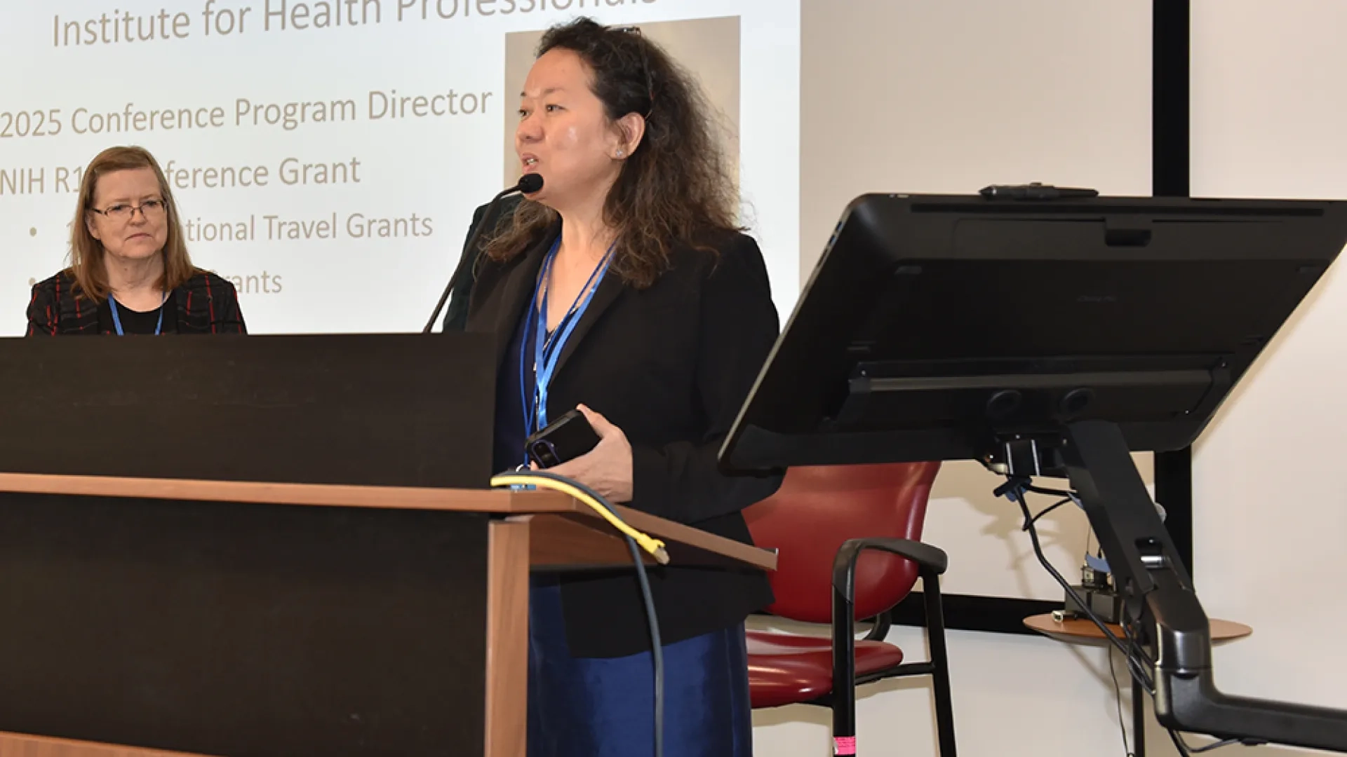 Woman stands podium, speaking into microphone