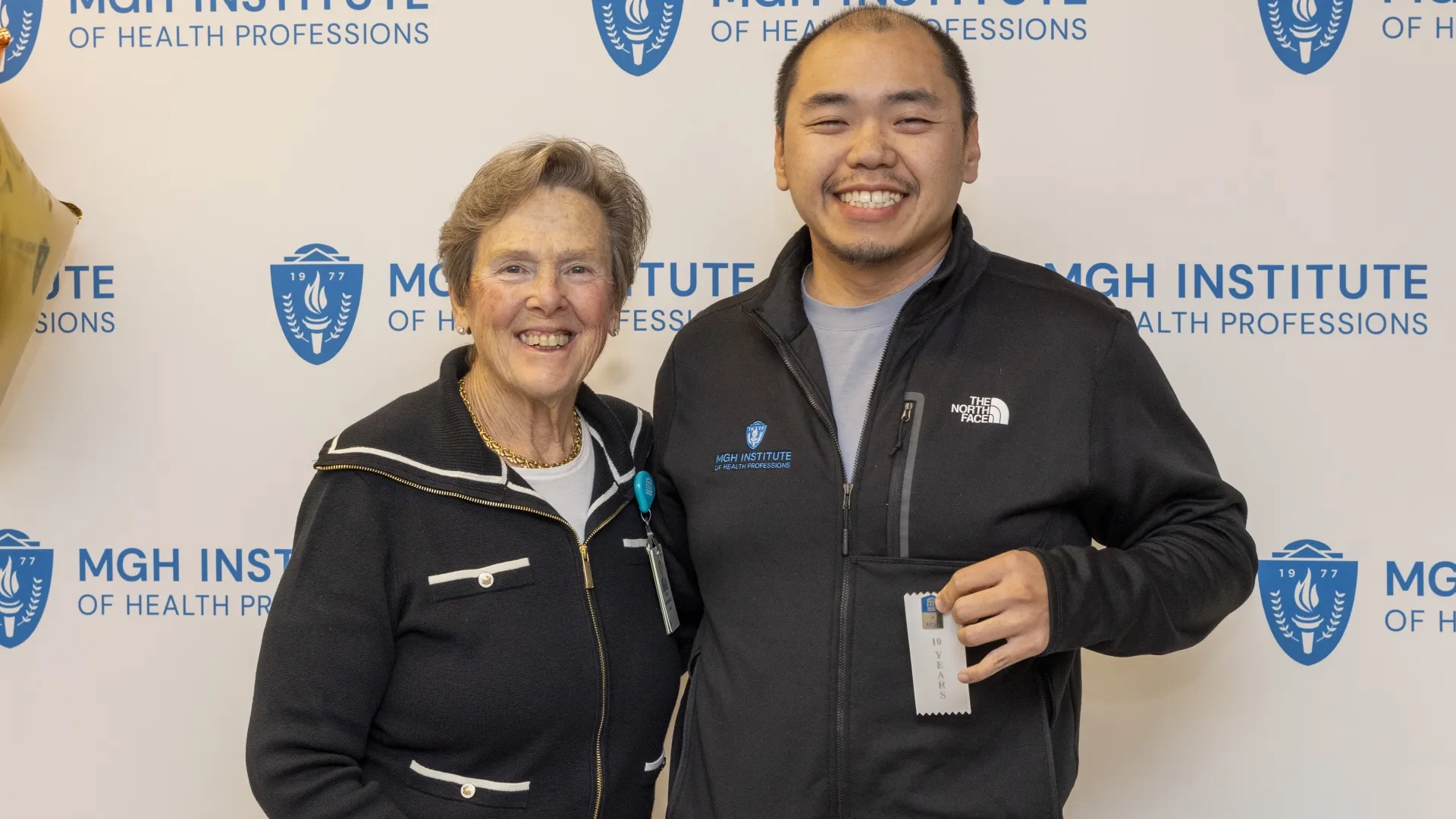 Two people pose in front of an MGH Institute backdrop