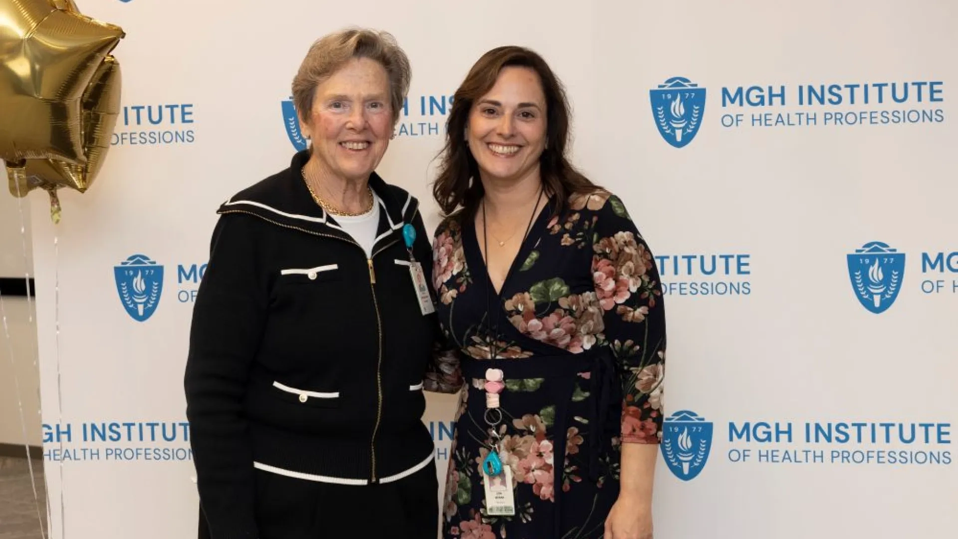 Two people pose in front of an MGH Institute backdrop