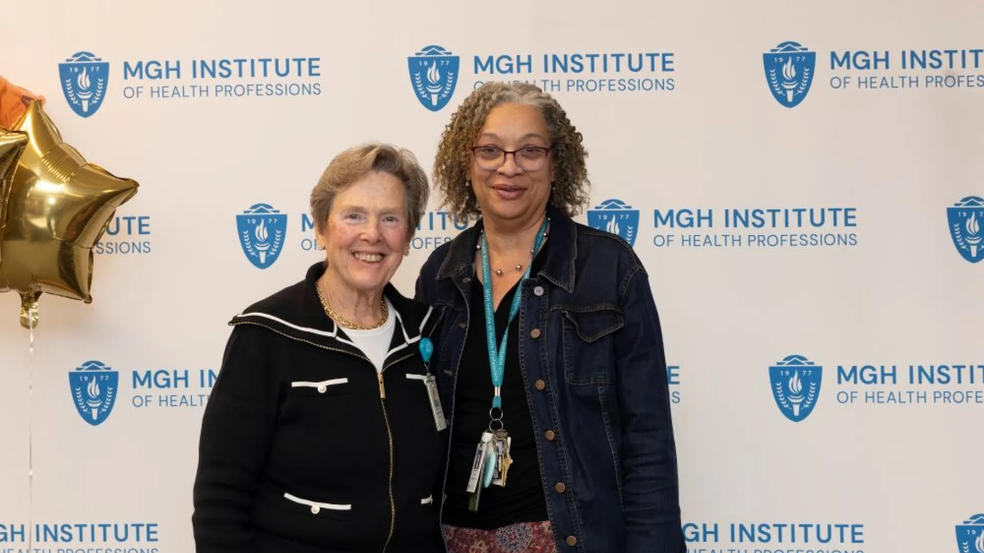 Two people pose in front of an MGH Institute backdrop