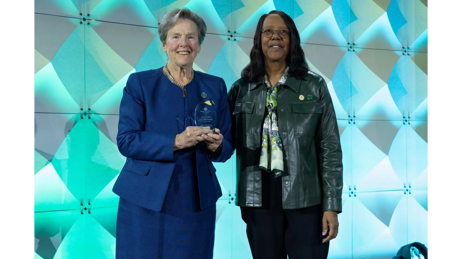 One woman holds a glass plaque while standing next to another woman