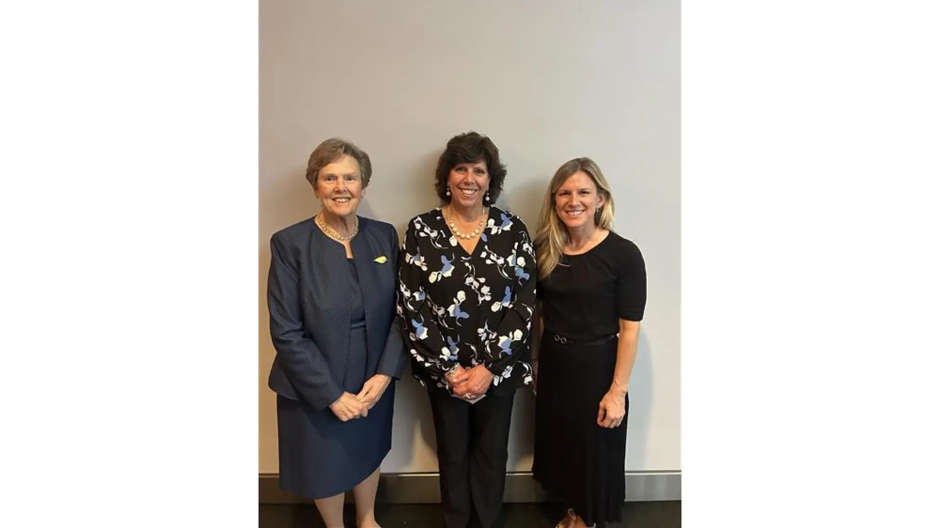 Three women pose while standing against a wall