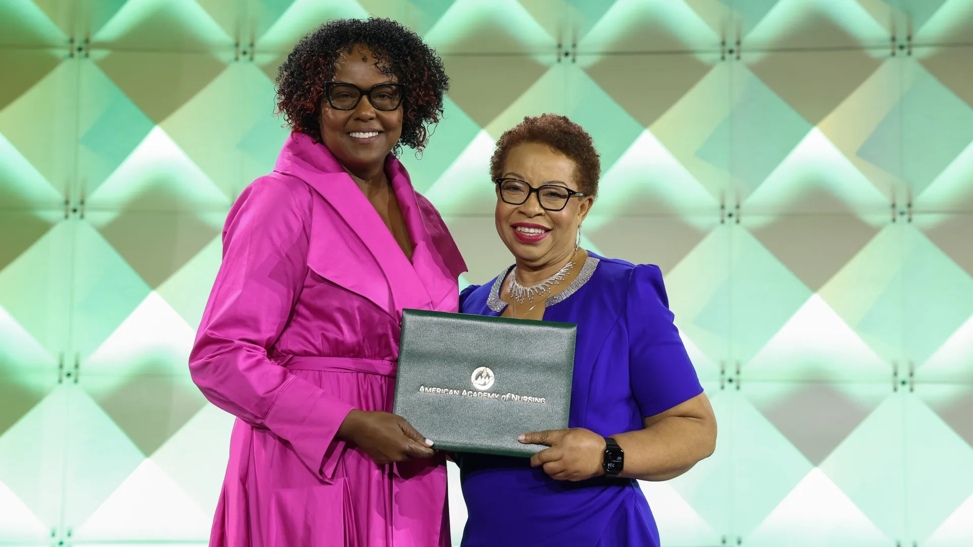 Two women pose holding a folder between them