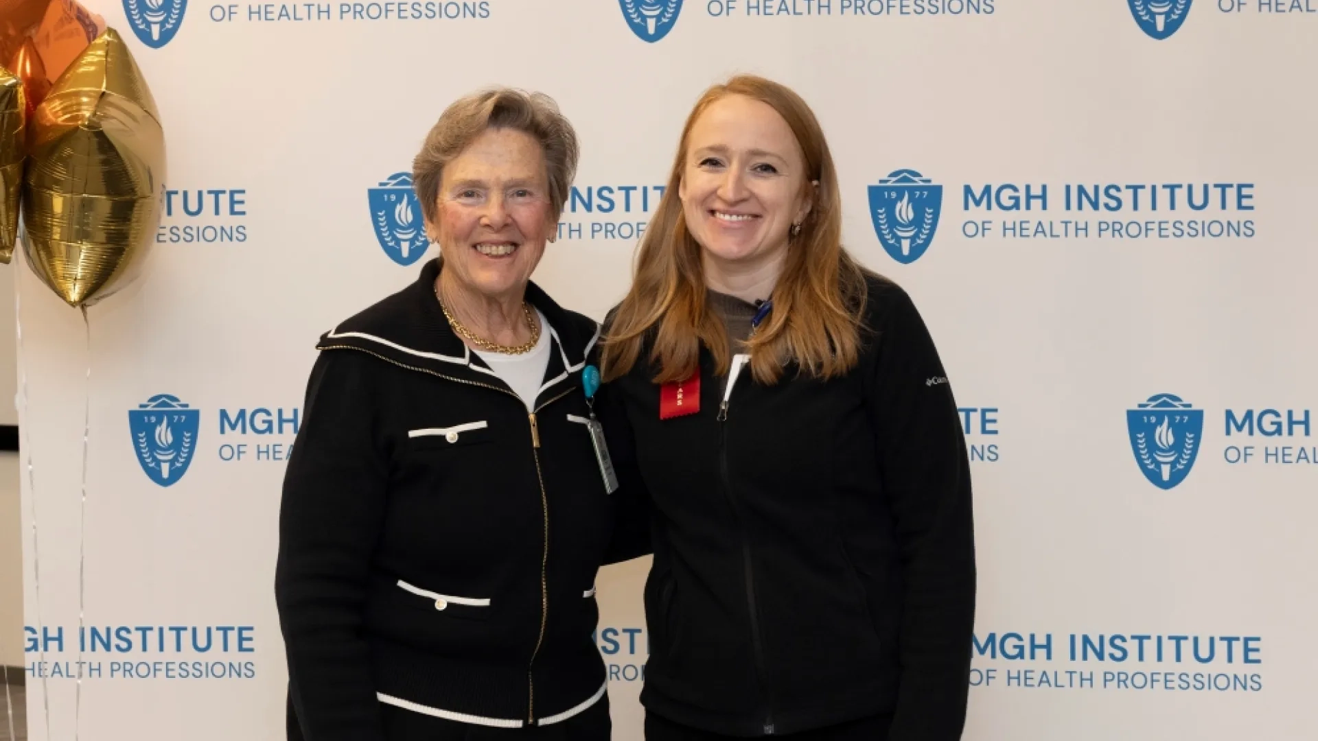 Two people pose in front of an MGH Institute backdrop