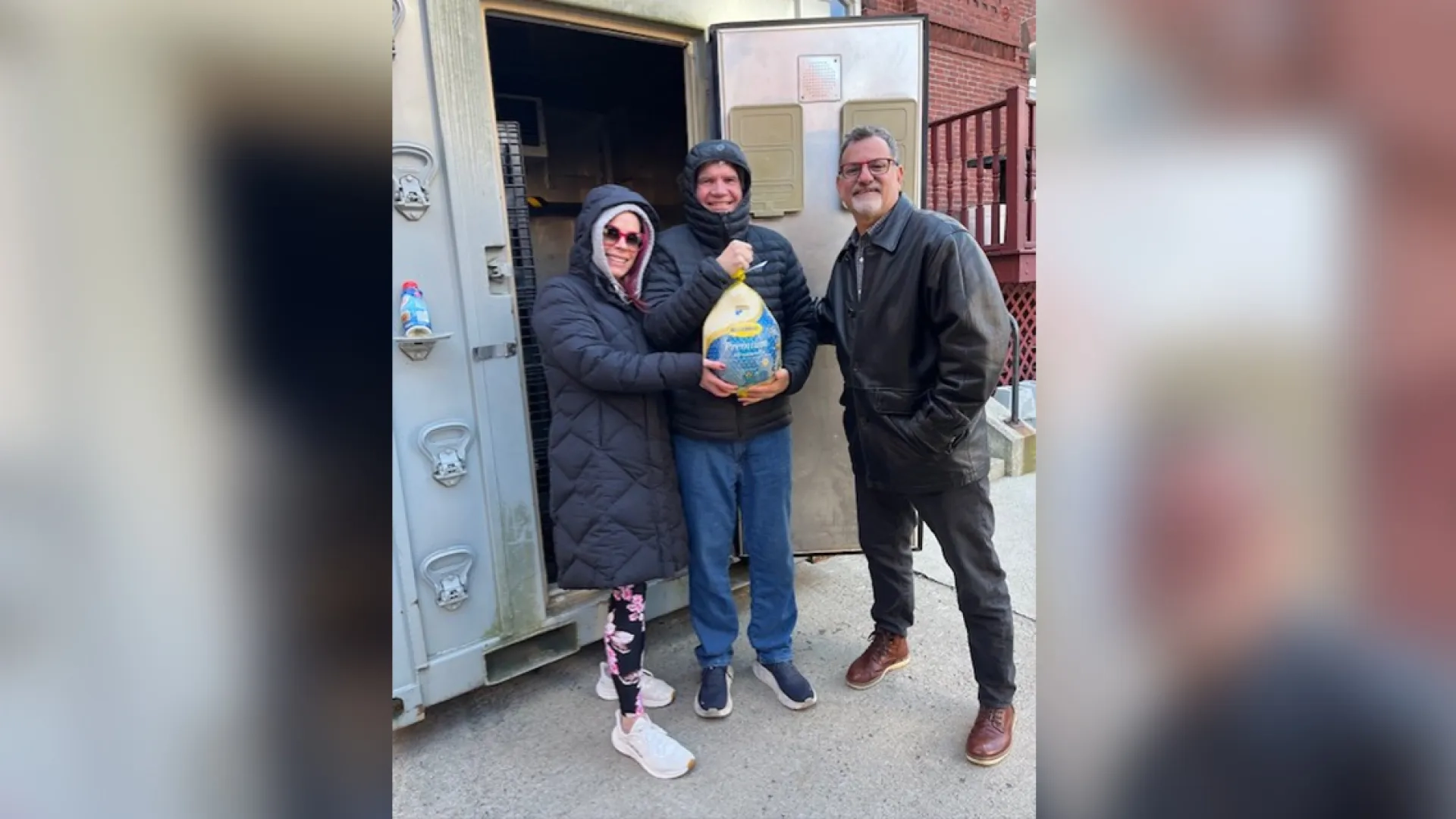 three people in front of a large walk in freezer hold a wrapped turkey