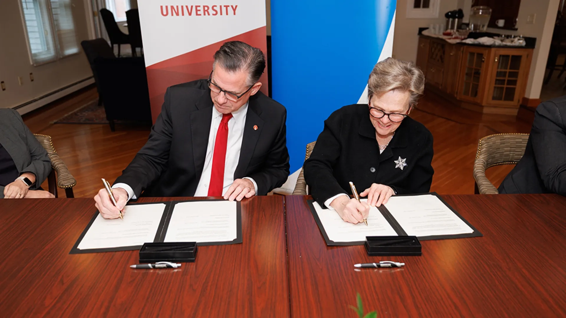 Two people sit at a table signing paper