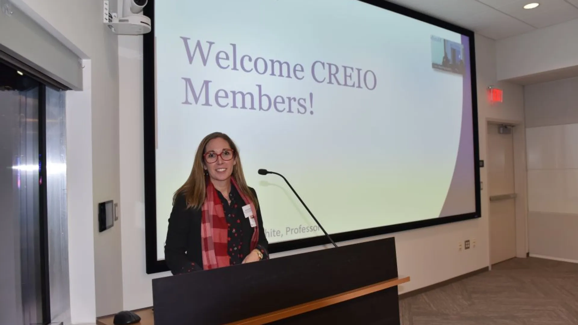 Woman at podium in front of a screen that reads Welcome CREIO members