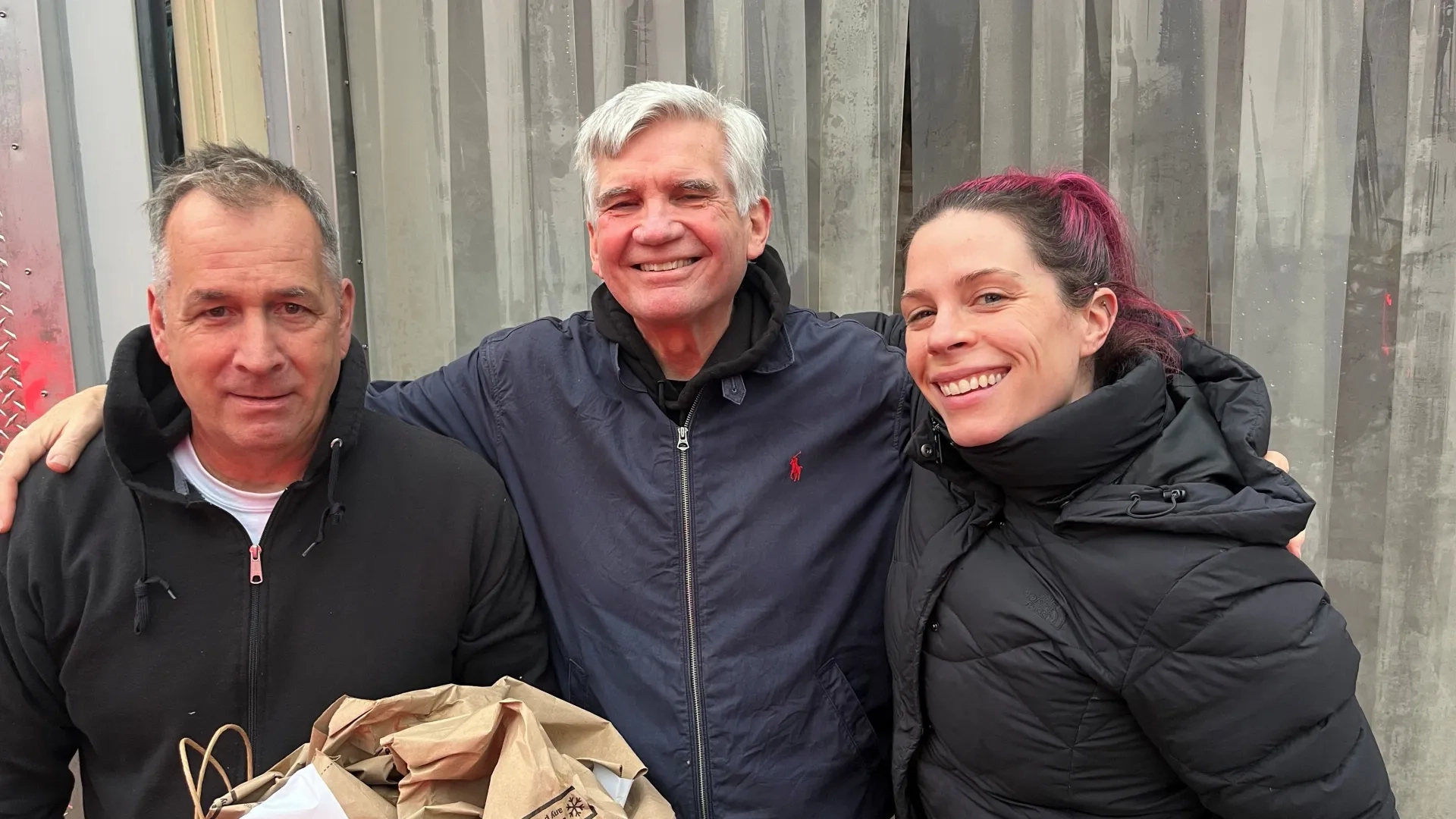 Three people pose for the camera with one holding paper bags