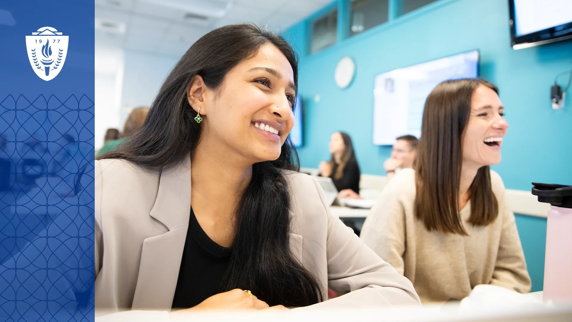Two women sitting in at a classroom desk and smiling