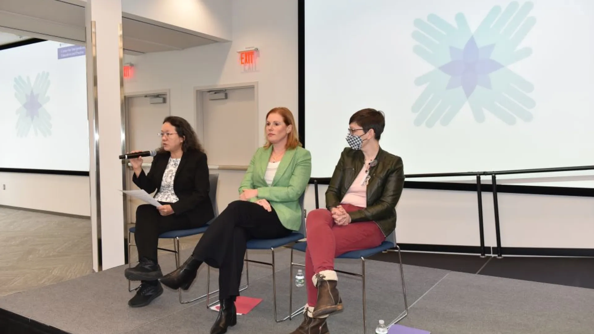 3 women sitting in chairs on a stage in front of a screen 
