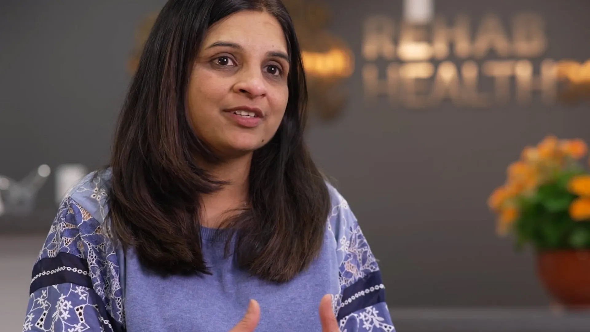 naseem wears a periwinkle patterned top and sits in the lobby of rehab health