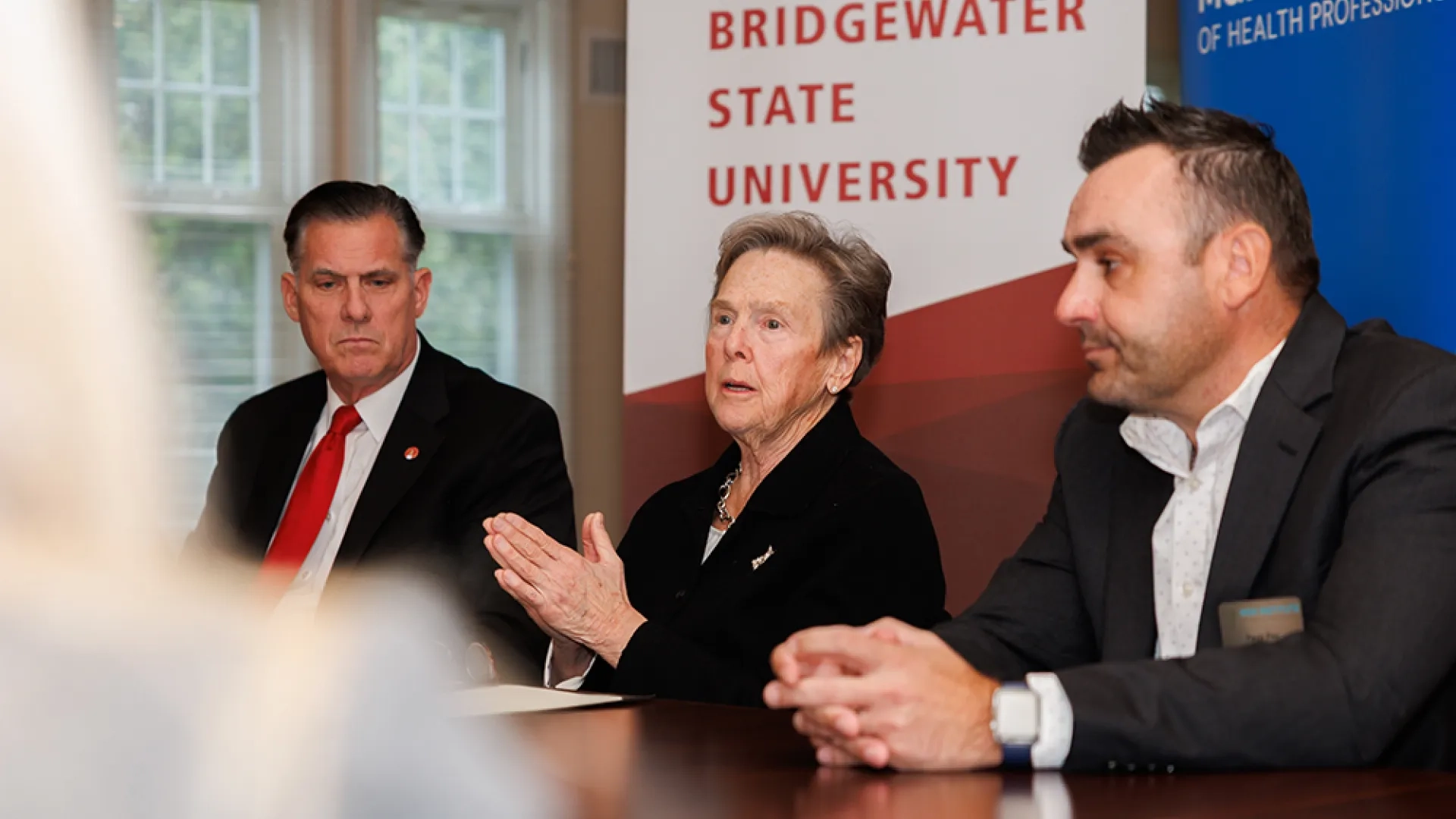 Three people sit at a table while the woman in the middle talks